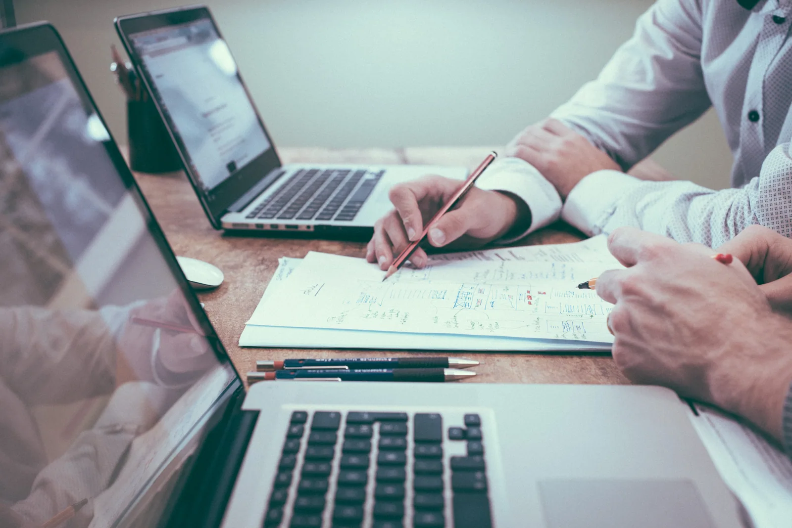 Two people connecting information in paper records beside their laptops